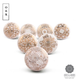 May include: Seven white ceramic cabinet knobs with gold floral patterns. The knobs feature diverse designs, including detailed flower and mandala-style motifs. The image includes the text "O & K" and "ODDS & KNOBS" with the tagline "SUPPLIERS OF HAND-PAINTED CERAMIC CABINET KNOBS."
