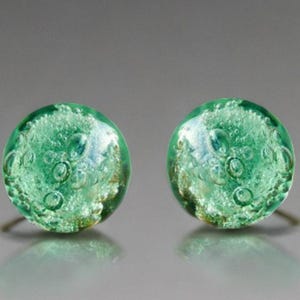 Op de afbeelding: Een paar ronde, groene oorstekers. Elke oorbel heeft een helder, bubbelachtig ontwerp met een zilveren pin. De oorbellen hebben een reflecterend oppervlak en zijn geplaatst tegen een neutrale achtergrond.