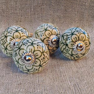 May include: Four decorative ceramic cabinet knobs. Each knob is off-white with a green floral pattern and a silver-coloured metal base. The knobs are round and have a glossy finish.