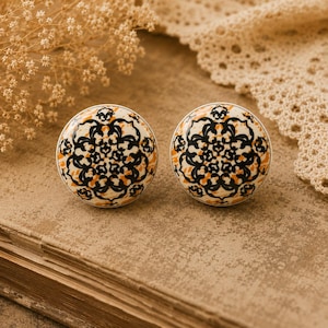 May include: Two round cabinet knobs with a cream background and a black and orange floral design. The knobs are made of ceramic and have a glossy finish. The knobs are approximately 3.8 cm in diameter.