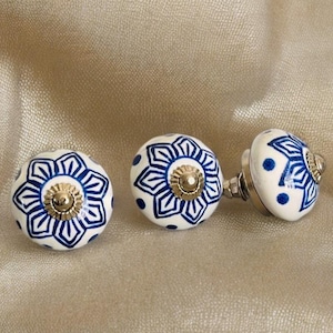 May include: Three white ceramic knobs with blue and gold floral designs. The knobs have a round shape and are perfect for adding a touch of elegance to any room.