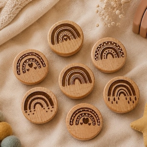 May include: Wooden rainbow-themed toys. Seven round wooden pieces with engraved rainbow designs, hearts, and stars. A wooden rainbow arch and a yellow star are also visible. The toys are arranged on a beige fabric surface.