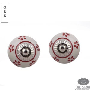 May include: Two white ceramic cabinet knobs with a red floral design and a silver metal center.
