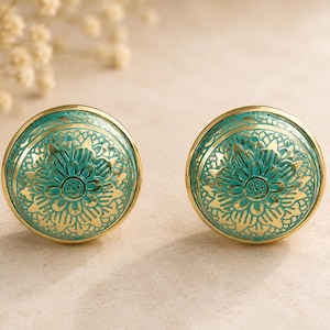 Può includere: Due pomelli decorativi per mobili. Ogni pomello presenta un motivo floreale turchese su una base dorata. I pomelli sono rotondi e probabilmente in metallo. Il motivo floreale è dettagliato e intricato.