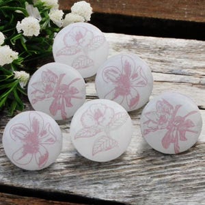 Puede incluir: Seis pomos de cerámica blanca con diseños florales rosas. Los pomos son redondos y tienen un acabado liso y brillante.