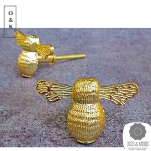 May include: Two gold bee-shaped cabinet knobs with detailed wings. The knobs are made of ceramic and have a textured finish.