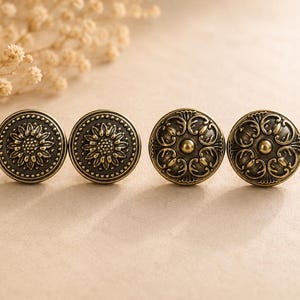 May include: Four antique brass cabinet knobs. Two knobs feature a sunflower design, while the other two have an ornate, swirling pattern. The knobs are round with a slightly raised design and a dark, aged finish.