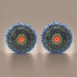 Może przedstawiać: Dwa niebieskie, dekoracyjne gałki do szafek z misternymi wzorami mandali. Gałki mają centralny pomarańczowy kwiat otoczony szczegółowymi wzorami w kolorze czerwonym, zielonym i ciemnoniebieskim. Idealne do dodania odrobiny stylu boho do mebli.