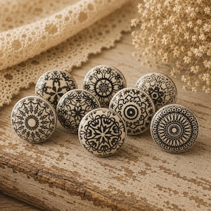 May include: Eight ceramic cabinet knobs with black and white decorative patterns. The knobs are round and feature symmetrical designs, including floral and geometric motifs. They are displayed on a weathered wooden surface.