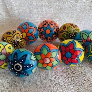 Peut inclure: Un ensemble de dix boutons en céramique colorés avec des motifs floraux complexes. Les boutons sont peints dans des tons de bleu, vert, jaune, orange et rouge.