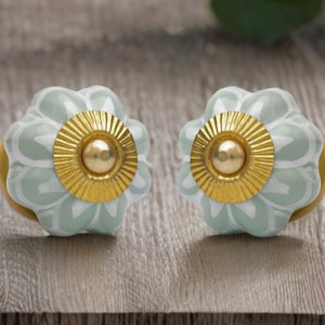 May include: Two decorative cabinet knobs. Each knob has a light blue and white floral design with a gold-coloured centre and base. The knobs are made of ceramic and metal.