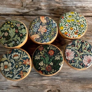 Puede incluir: Seis posavasos redondos con diseños florales en varios colores, incluyendo verde, azul, naranja y rosa. Los posavasos tienen un borde de madera y están dispuestos sobre una superficie de madera. Los diseños presentan motivos botánicos y de la naturaleza.