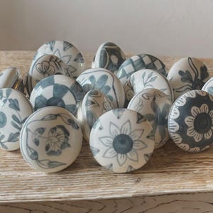 May include: A collection of ceramic cabinet knobs with various blue and white floral and geometric patterns. The knobs are round and have a glossy finish, perfect for adding a decorative touch to furniture.