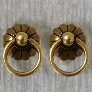 May include: A pair of antique brass drawer pulls. Each pull has a floral-shaped backplate, a central knob, and a circular handle. The pulls are made of shiny, golden-coloured metal. They are set against a neutral background.