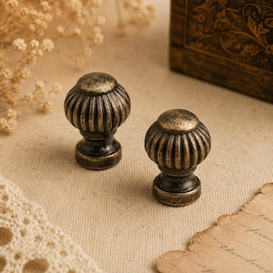 Op de afbeelding: Twee antiek bronzen kastknoppen met een geribbeld, afgerond ontwerp. De knoppen hebben een donkere basis en een lichtere, verouderde afwerking aan de bovenkant. Deze decoratieve knoppen zijn ideaal om een vintage touch aan meubels toe te voegen.