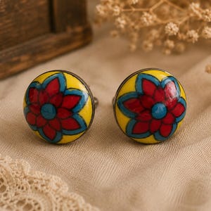 May include: Two decorative cabinet knobs with a floral design. Each knob features a yellow background with a red and blue flower design. The knobs are round and have a metal base, perfect for adding a pop of color to furniture.