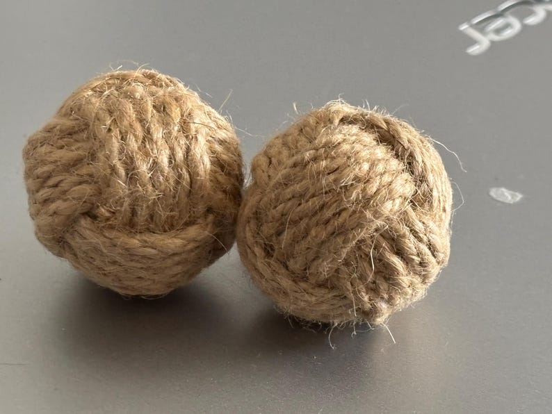 Pode incluir: Duas bolas decorativas de corda em estilo n&aacute;utico. As bolas s&atilde;o feitas de corda de cor natural, fortemente enrolada e amarrada em forma redonda. A textura da corda &eacute; vis&iacute;vel. Est&atilde;o sobre uma superf&iacute;cie cinza.