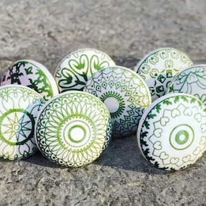 May include: Set of eight green and white ceramic knobs with intricate mandala designs. The knobs are round and have a raised edge. They are perfect for adding a touch of bohemian style to your home decor.