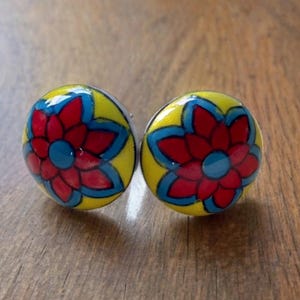 May include: A pair of yellow and red floral earrings with blue accents. The earrings are round and have a glossy finish.