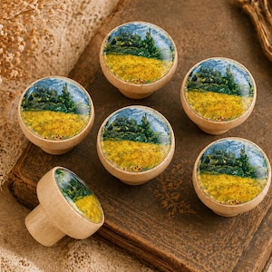 May include: Six wooden cabinet knobs with a landscape design featuring a yellow field, green trees, and a blue sky. The knobs are round with a light wood finish, and one knob is shown separately.