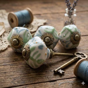 May include: A collection of decorative ceramic cabinet knobs with brass hardware. The knobs feature a white base with green and blue floral patterns. A vintage key and spools of thread are also present.