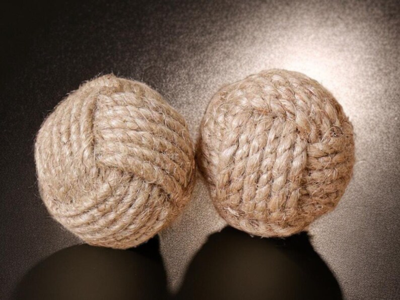 Pode incluir: Dois objetos decorativos esf&eacute;ricos feitos de corda natural bem enrolada. A corda &eacute; de cor castanho claro e as esferas est&atilde;o sobre uma superf&iacute;cie escura. Os objetos t&ecirc;m uma est&eacute;tica n&aacute;utica ou r&uacute;stica.