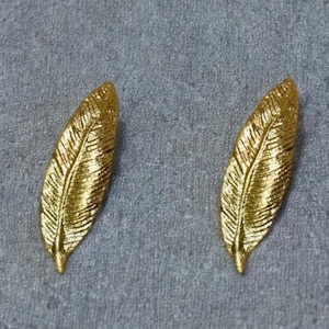 May include: A pair of gold leaf-shaped earrings. The earrings are made of metal and have a textured surface.