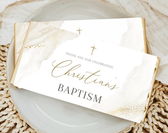 May include: Two rectangular baptism favors with gold accents and the text "Thank you for celebrating Christian's Baptism" are displayed on a white plate. The favors have a watercolor design and a cross.