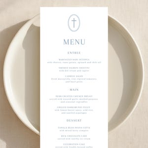 May include: A menu card with a light blue cross icon at the top, listing entree, main, and dessert options. The menu is on a white plate, with a light beige background.