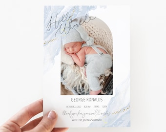 May include: A blue and white watercolor announcement card with gold glitter accents. The card features a photo of a baby boy sleeping in a knitted hat. The text reads "Hello World" and "George Ronalds" with the baby's birth date, time, weight, and length. The card also includes the text "Thank you for your well wishes" and "With love Jason & Savannah."