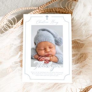 Könnte beinhalten: Baby-Dankeskarte zur Taufe mit einem Foto eines schlafenden Säuglings in einem blauen Hut und Outfit. Die Karte hat einen blauen Rand und den Text "Christian Harry" und "Thank you".