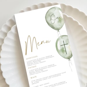 Może przedstawiać: Biała karta menu ze złotym napisem „Menu”. Karta zawiera dwa zielone akwarelowe balony ze słowem „One” i krzyżem. Menu zawiera przystawki, dania główne i dania główne.