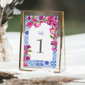 May include: A white table number card with a pink floral border and blue and white tile pattern. The card reads "Table 1".