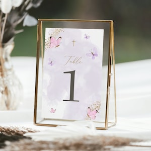 Op de afbeelding: Een tafelnummerkaart met een paarse aquarel achtergrond en gouden glitter accenten. De kaart heeft een gouden kruis, de tekst "Tafel 1" en roze vlinders.
