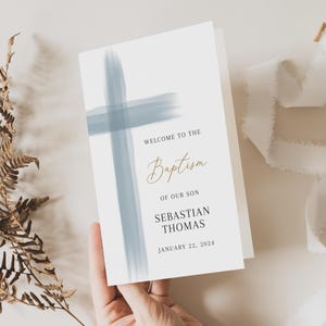 May include: A white card with a blue watercolour cross design. The text reads "Welcome to the Baptism of our son Sebastian Thomas January 22, 2024".