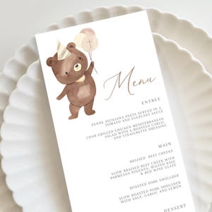 Pode incluir: Um cartão de menu com uma ilustração em aquarela de um urso marrom usando um chapéu de festa e balões. O menu apresenta opções de entrada, prato principal e sobremesa, com texto em uma fonte delicada.