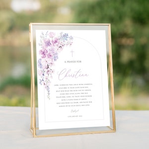 May include: A white card with a purple floral design and a cross at the top. The card has a prayer for Christina, with the text "Lord, surround this child with goodness, lead her in your light each day, help her walk the path you've chosen, guide her steps along the way, teach her, Lord, to trust your wisdom with a faith from up above, keep her from all harm, and bless her always with your grace and love." The card also includes the date "15th January 2024" and the word "Baptized".