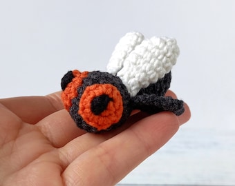 May include: A crocheted fly toy with black and gray body, orange and black eyes, and white wings.