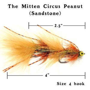 May include: A brown and orange fly fishing lure with a yellow eye, called "The Mitten Circus Peanut (Sandstone)". The lure is 4 inches long and has a size 4 hook.