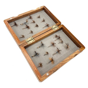 Peut inclure: Une boîte de pêche à la mouche en bois avec deux compartiments à charnières. Chaque compartiment est doublé de feutre gris et contient une variété de mouches.