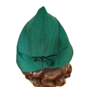 Può includere: Un cappello verde scuro, a punta, con un fiocco sul retro. Il cappello è fatto di un tessuto liscio e ha un design semplice.