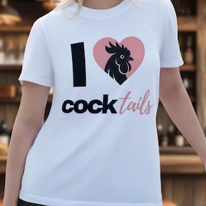 Peut inclure: T-shirt blanc avec l'inscription "I Cocktails" en noir et rose. Le design comprend une ligne verticale noire, un cœur rose et une silhouette de coq noir. Le t-shirt a des manches courtes.