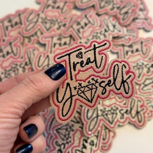May include: A close-up of a pink and white glitter iron-on patch with black embroidery that reads "Treat Yourself" with a diamond graphic.