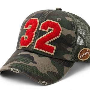 May include: A camouflage print trucker hat featuring a distressed brim and the number 32 in red felt with gold stitching on the front. The side of the hat displays an oval patch with a brown football graphic and white stitching details.