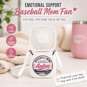 May include: A white portable neck fan with a square base featuring a circular graphic that reads BASEBALL MOM, EMOTIONAL SUPPORT FAN, Andrea, FOR STRESSFUL INNINGS & QUESTIONABLE CALLS. The fan includes a white strap and has three speed settings.