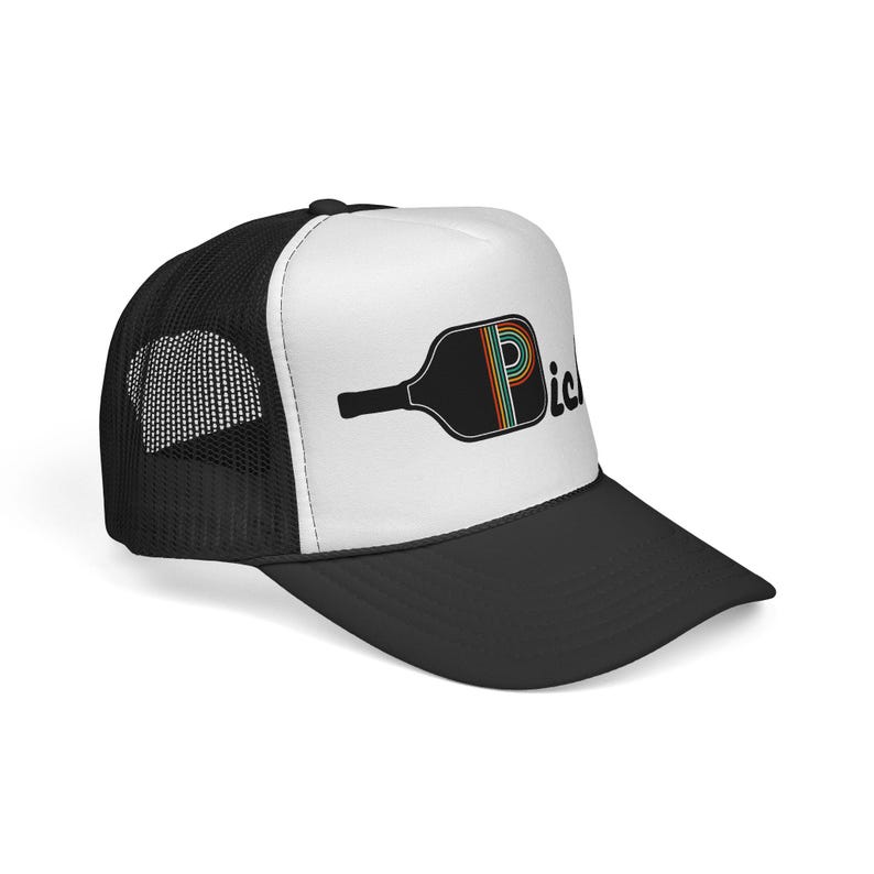 May include: A black and white trucker hat featuring a graphic of a black pickleball paddle with a colorful rainbow-striped letter P on the front panel. The hat has a solid black brim, a white front panel, and a black mesh back for ventilation.