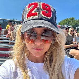 May include: A distressed charcoal gray baseball cap featuring the number 29 in red chenille fabric with gold trim on the front panel. The cap has a structured crown, a curved brim with frayed edges, and a mesh back panel for ventilation.