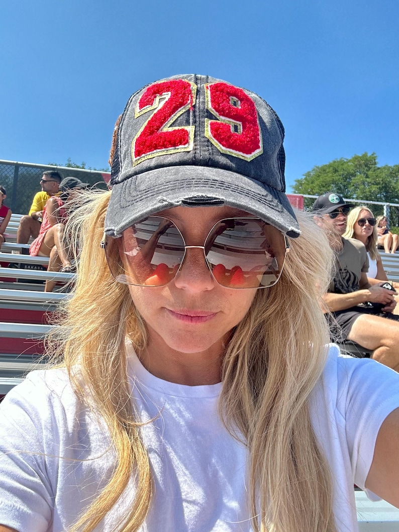 May include: A distressed charcoal gray baseball cap featuring the number 29 in red chenille fabric with gold trim on the front panel. The cap has a structured crown, a curved brim with frayed edges, and a mesh back panel for ventilation.