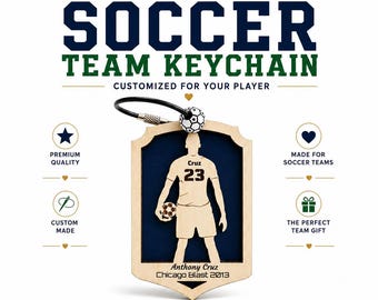 May include: A personalized wooden soccer keychain featuring a shield-shaped frame with a dark blue background. The center displays a light-colored soccer player silhouette with the name Cruz and number 23, plus a soccer ball bead on a black ring.