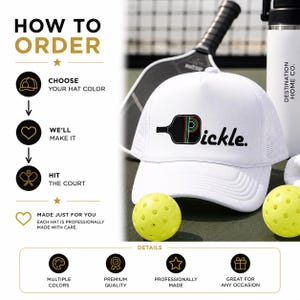 May include: A white trucker hat featuring a graphic of a black pickleball paddle with a rainbow-striped letter P and the text pickle. The hat is displayed alongside two yellow perforated pickleballs, a paddle, and a white water bottle.
